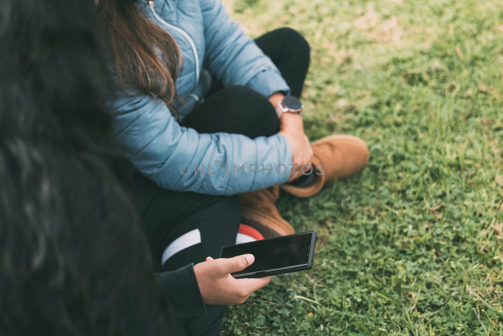 group of three Hispanic friends enjoying a beautiful day in the park, while bonding over their shared love of technology. The photo is taken from a side view, so their faces are not visible, but we can see them sitting on the ground, with one of the young men holding a smartphone, which they all seem to be looking at. social aspects of technology use in modern society, as well as the importance of spending time outdoors and sharing experiences with friends. comcept friendship, leisure time, technology use, and multiculturalism.