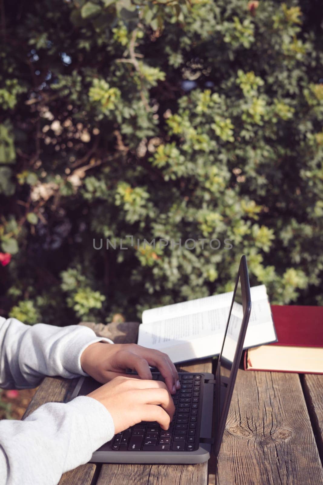 detail of hands typing on laptop with copy space, young latin man working outdoors in park with laptop and books, sitting on wooden bench