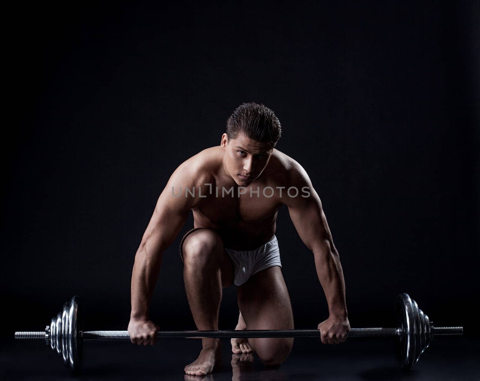 Sexual muscular guy posing with barbell in studio, isolated on black