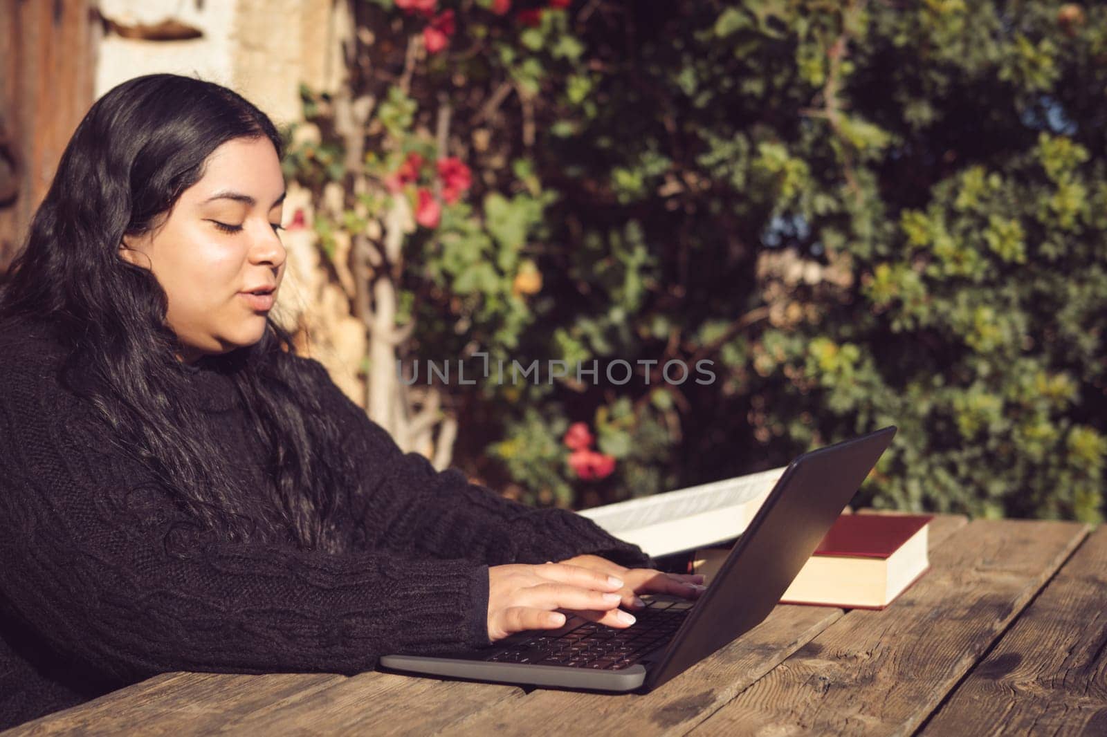 latin woman with long dark hair, typing on her laptop, working on a university educational project, outside in the park on the university campus.