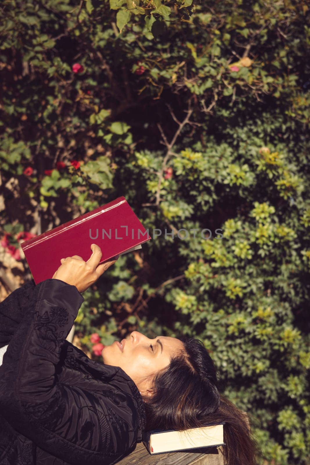 beautiful woman reading in garden, lying on wooden table takes vertical foreground copy space,