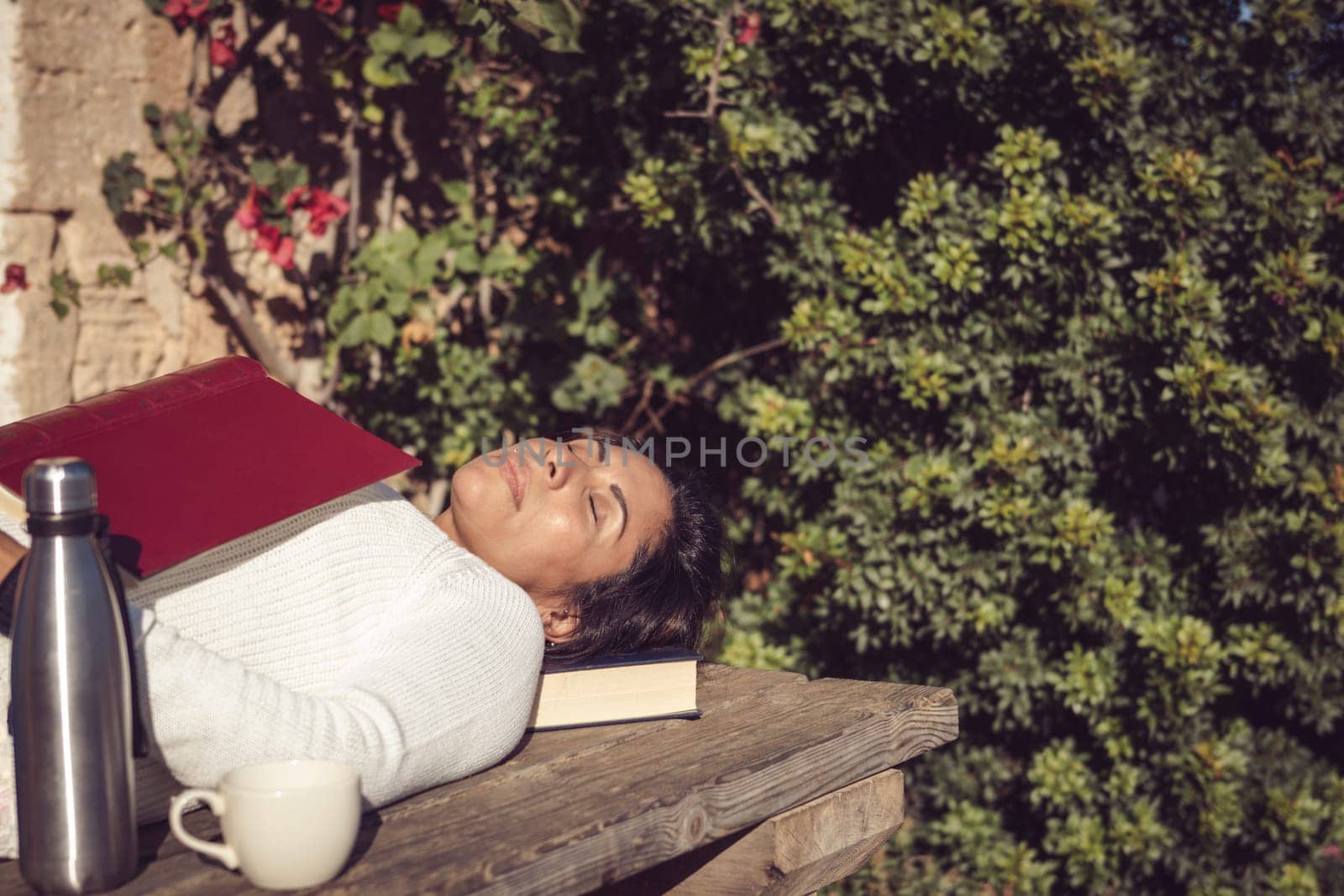 latin woman sleeping in the sun with a book on a wooden table in the garden of the house