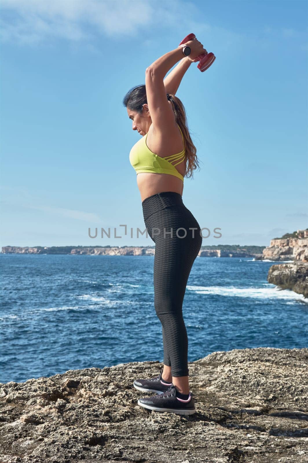 Latin woman, middle-aged, wearing sportswear, training, doing physical exercises, plank, sit-ups, climber's step, burning calories, keeping fit, outdoors by the sea, wearing headphones, smart watch