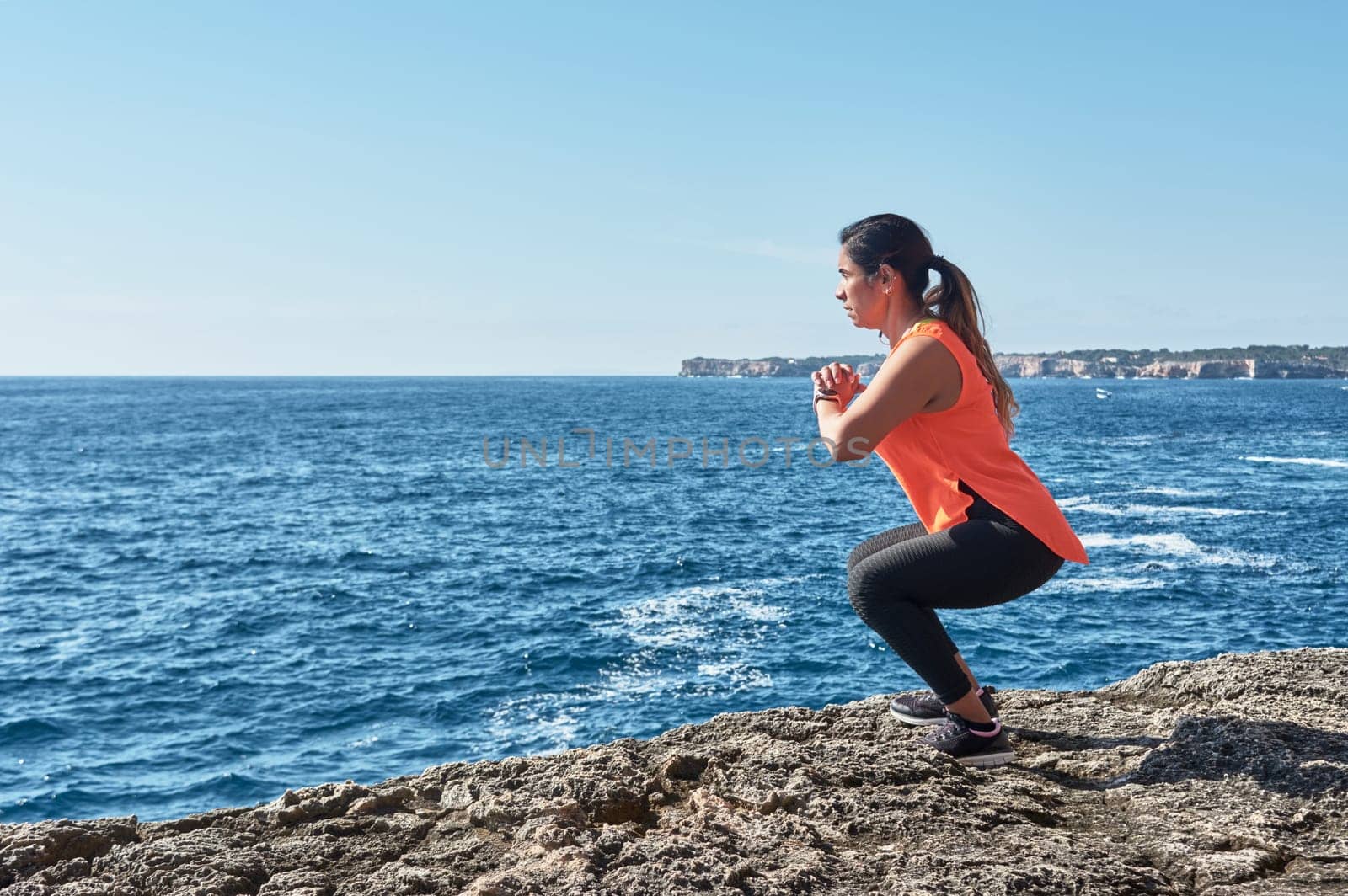 Latin woman, middle-aged, wearing sportswear, training, doing physical exercises, plank, sit-ups, climber's step, burning calories, keeping fit, outdoors by the sea, wearing headphones, smart watch