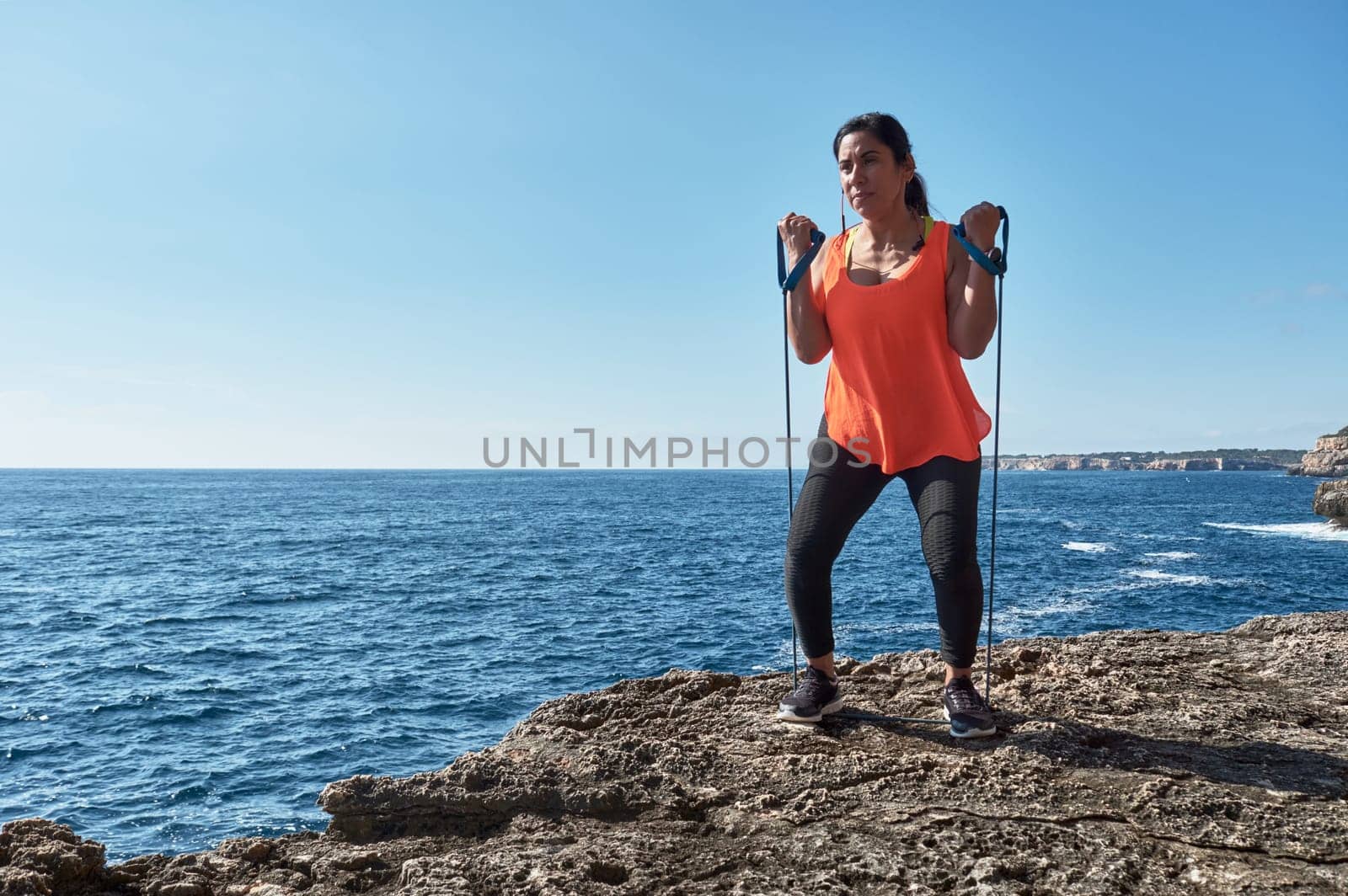 Latin woman, middle-aged, wearing sportswear, training, doing physical exercises, plank, sit-ups, climber's step, burning calories, keeping fit, outdoors by the sea, wearing headphones, smart watch