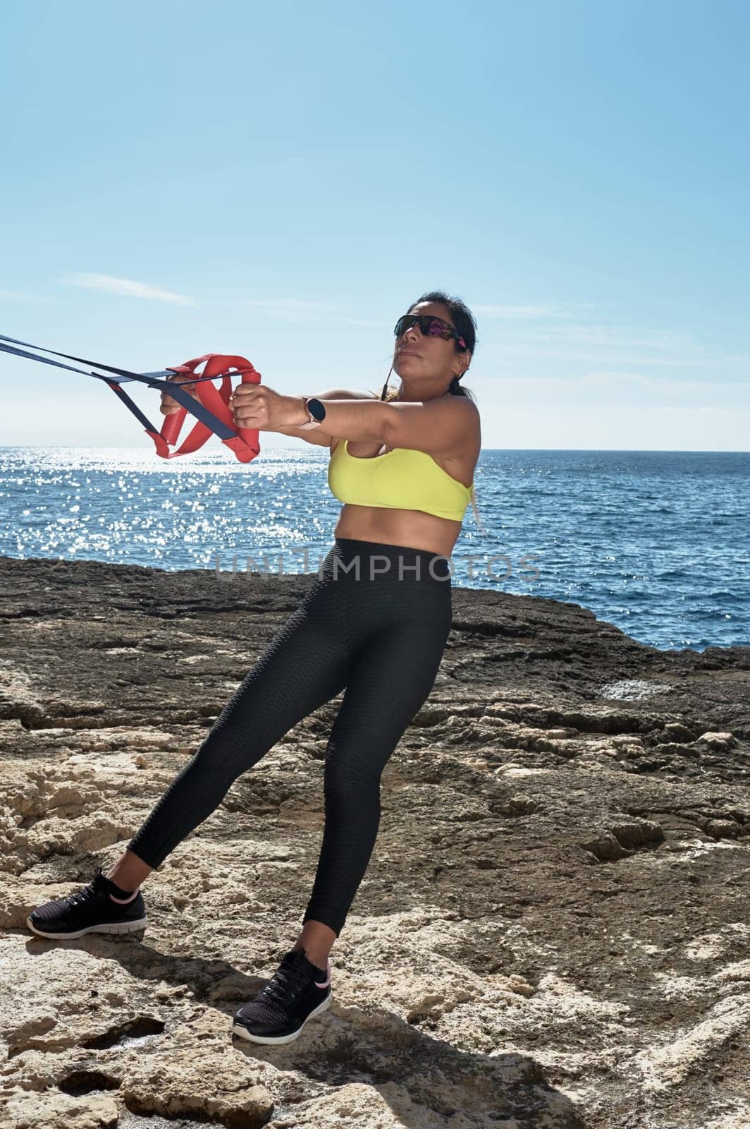 Latin woman, middle-aged, wearing sportswear, training, doing physical exercises, plank, sit-ups, climber's step, burning calories, keeping fit, outdoors by the sea, wearing headphones, smart watch