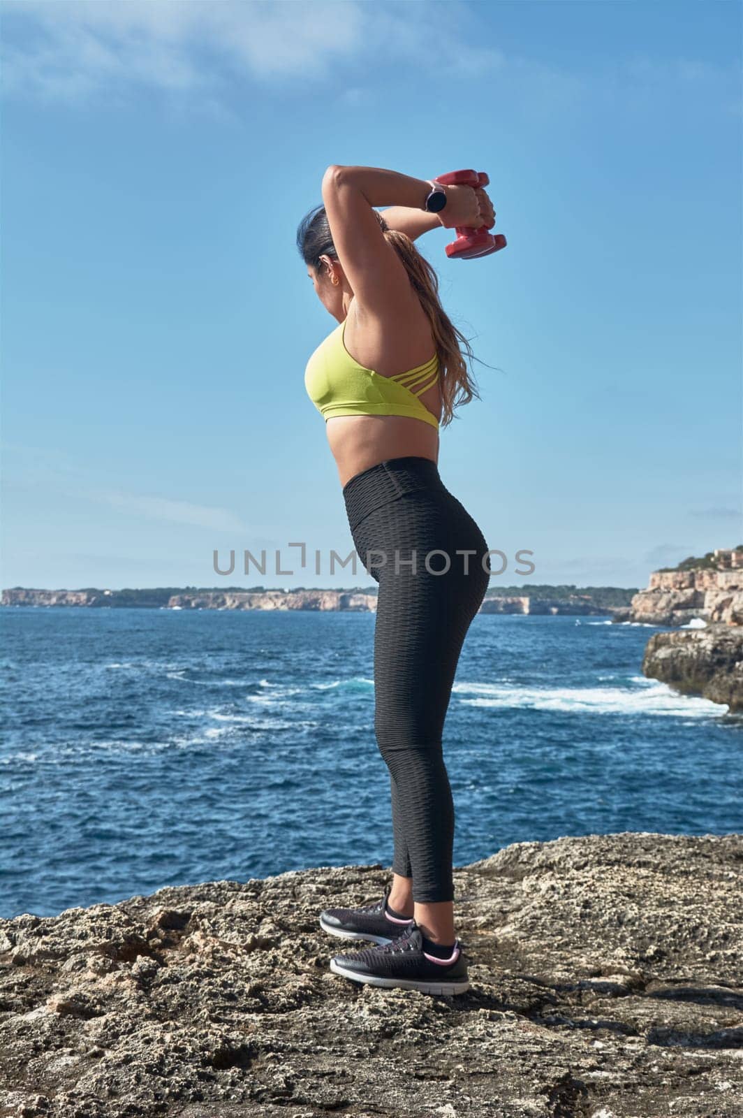 Latin woman, middle-aged, wearing sportswear, training, doing physical exercises, plank, sit-ups, climber's step, burning calories, keeping fit, outdoors by the sea, wearing headphones, smart watch