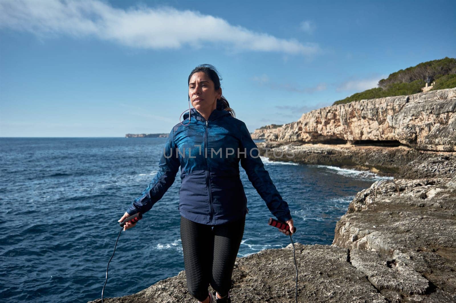 Latin woman, middle-aged, wearing sportswear, training, doing physical exercises, plank, sit-ups, climber's step, burning calories, keeping fit, outdoors by the sea, wearing headphones, smart watch