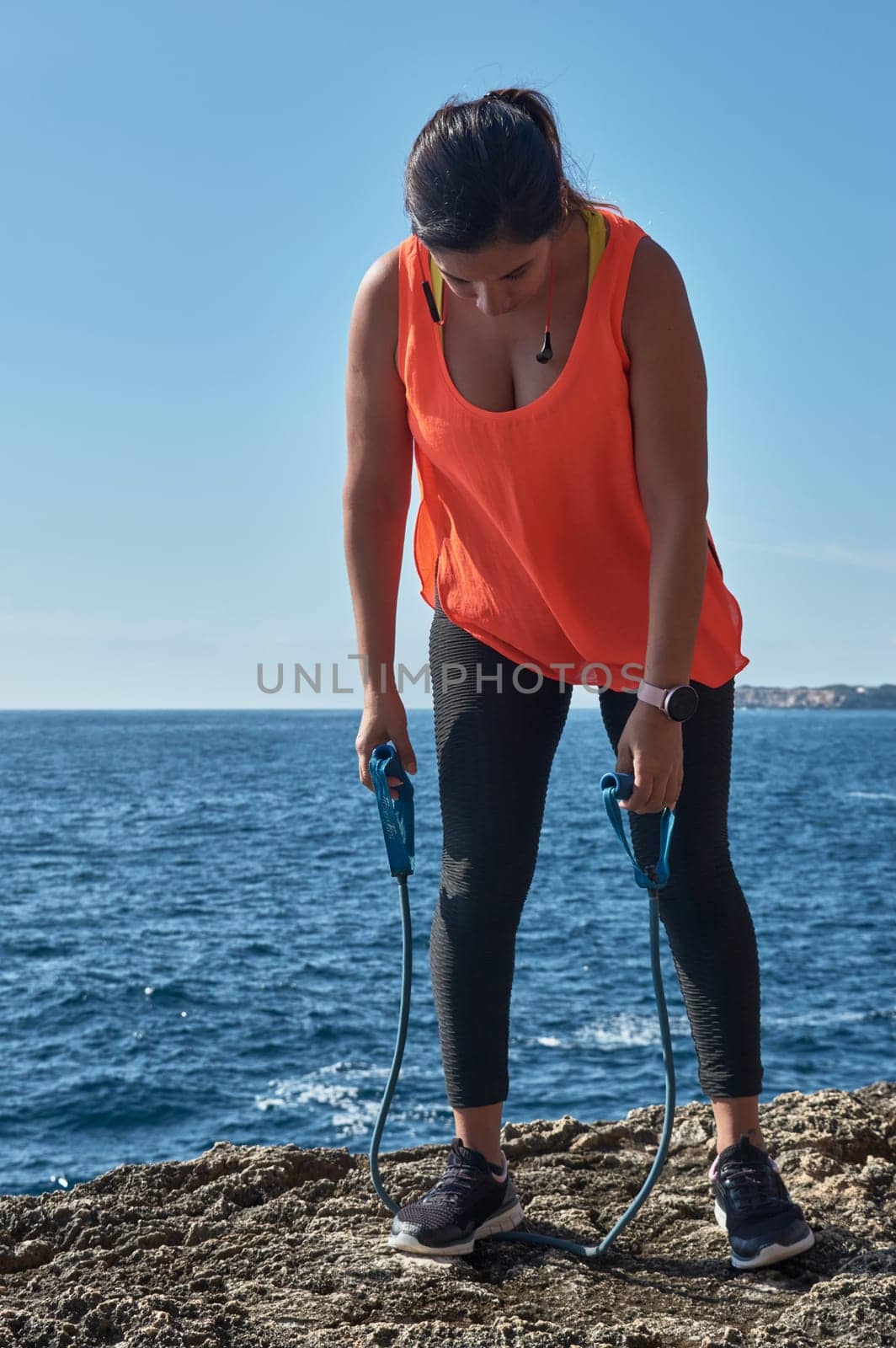 Latin woman, middle-aged, wearing sportswear, training, doing physical exercises, plank, sit-ups, climber's step, burning calories, keeping fit, outdoors by the sea, wearing headphones, smart watch