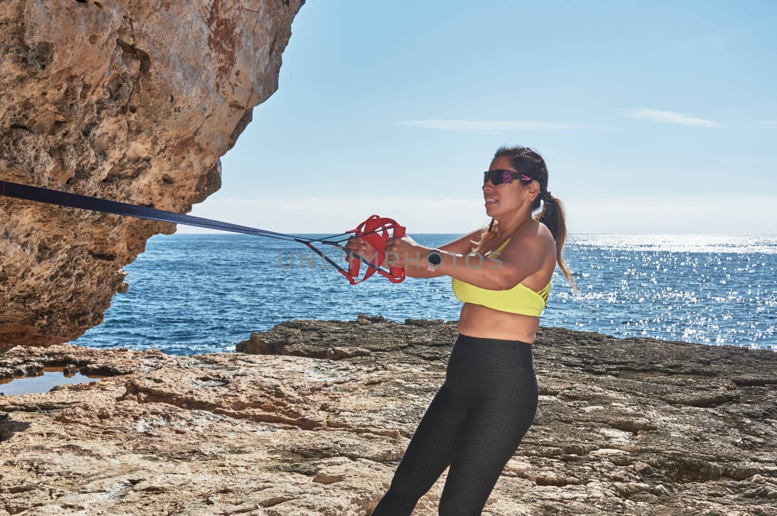 Latin woman, middle-aged, wearing sportswear, training, doing physical exercises, plank, sit-ups, climber's step, burning calories, keeping fit, outdoors by the sea, wearing headphones, smart watch