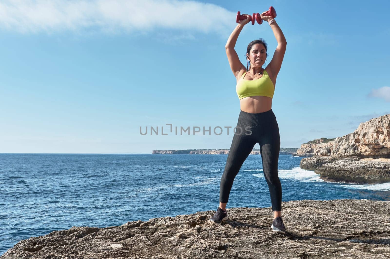 Latin woman, middle-aged, wearing sportswear, training, doing physical exercises, plank, sit-ups, climber's step, burning calories, keeping fit, outdoors by the sea, wearing headphones, smart watch