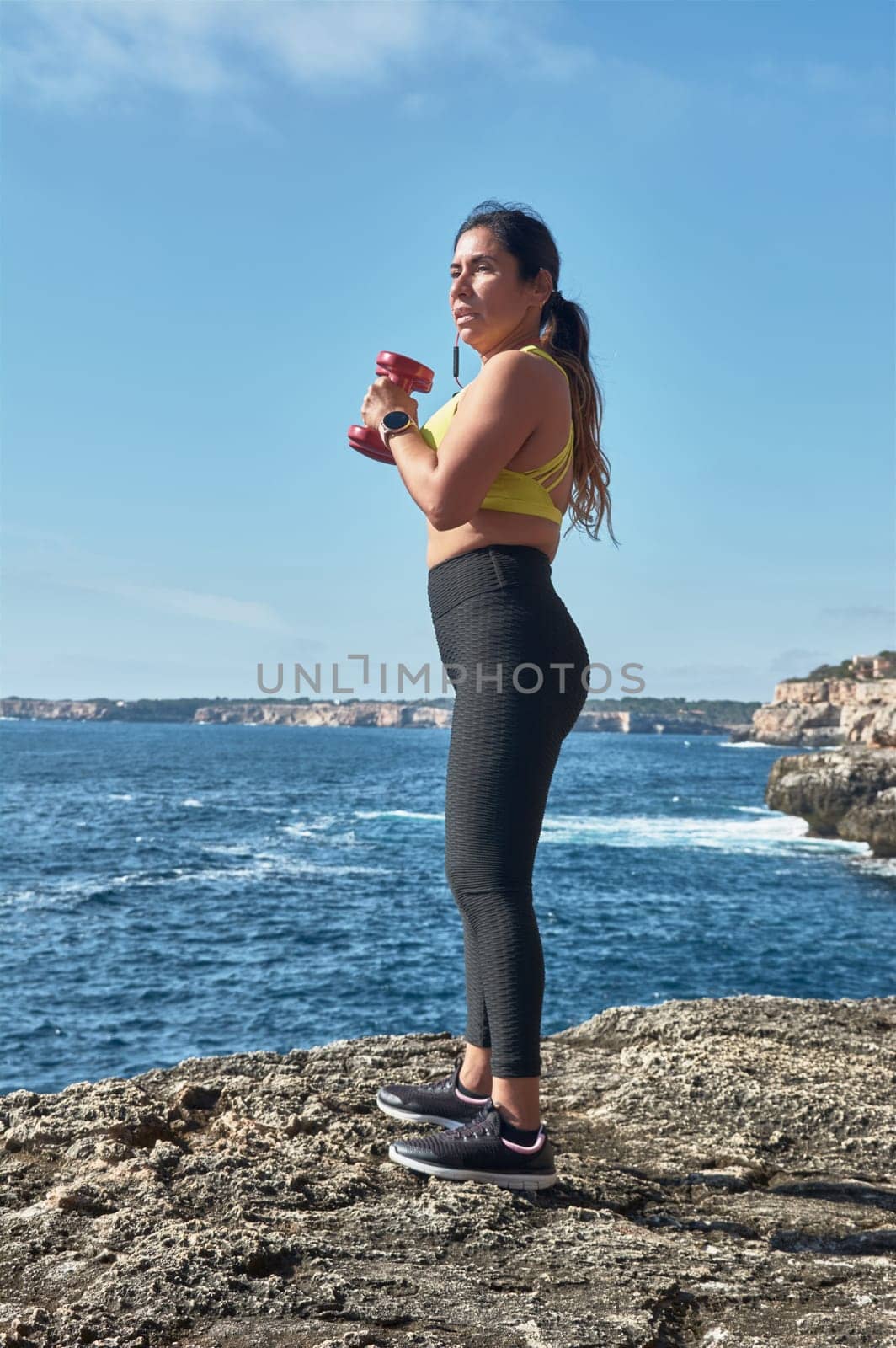 Latin woman, middle-aged, wearing sportswear, training, doing physical exercises, plank, sit-ups, climber's step, burning calories, keeping fit, outdoors by the sea, wearing headphones, smart watch