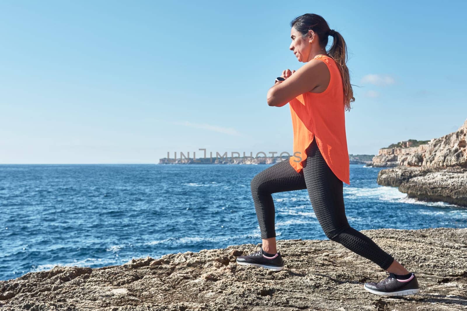 Latin woman, middle-aged, wearing sportswear, training, doing physical exercises, plank, sit-ups, climber's step, burning calories, keeping fit, outdoors by the sea, wearing headphones, smart watch