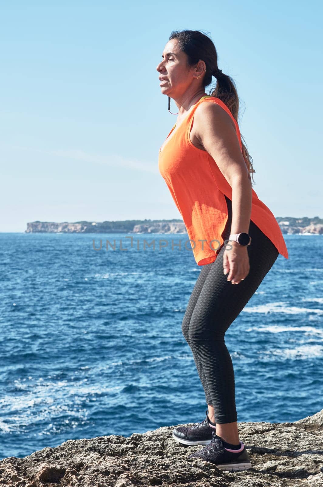 Latin woman, middle-aged, wearing sportswear, training, doing physical exercises, plank, sit-ups, climber's step, burning calories, keeping fit, outdoors by the sea, wearing headphones, smart watch