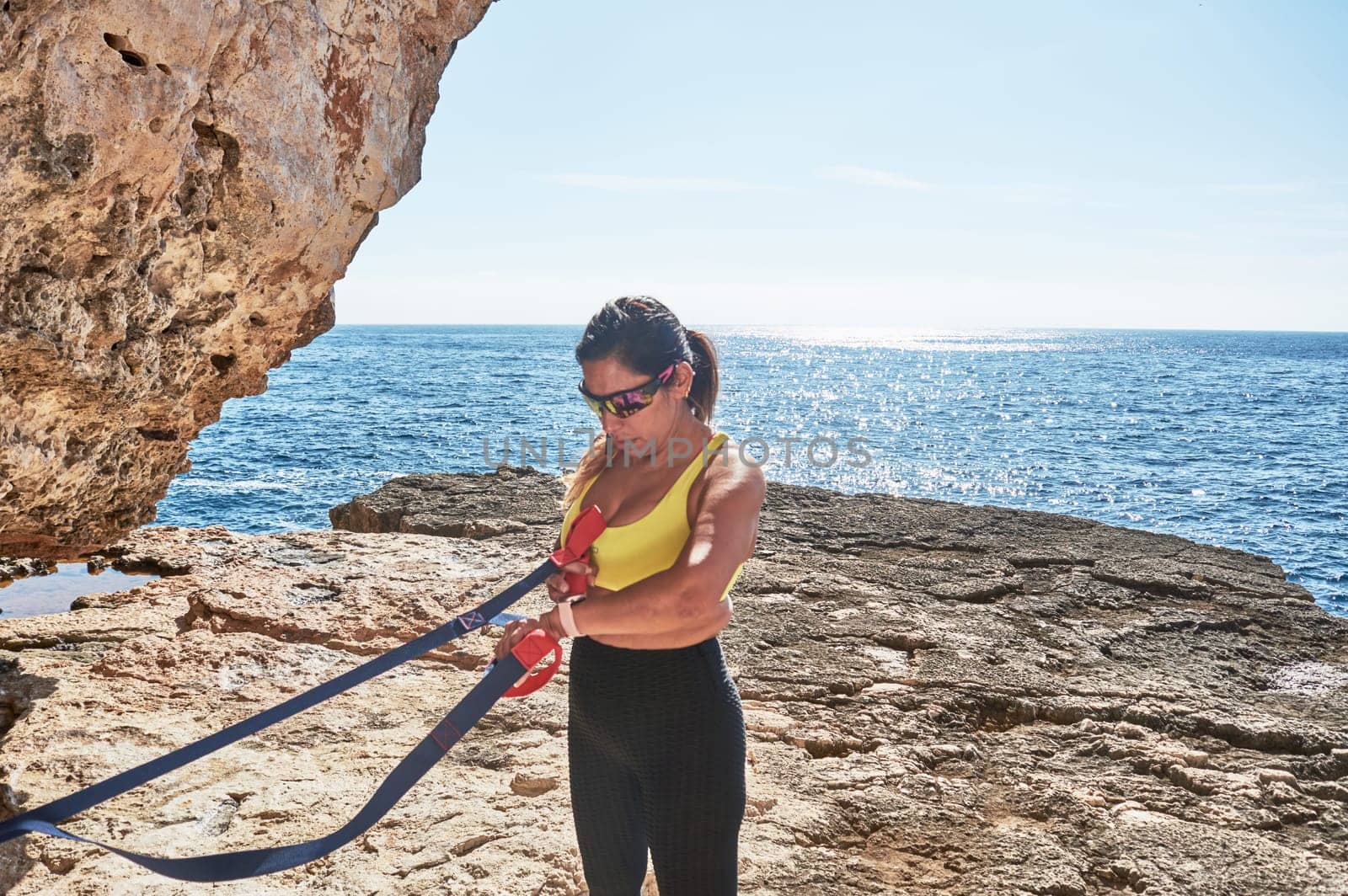 Latin woman, middle-aged, wearing sportswear, training, doing physical exercises, plank, sit-ups, climber's step, burning calories, keeping fit, outdoors by the sea, wearing headphones, smart watch