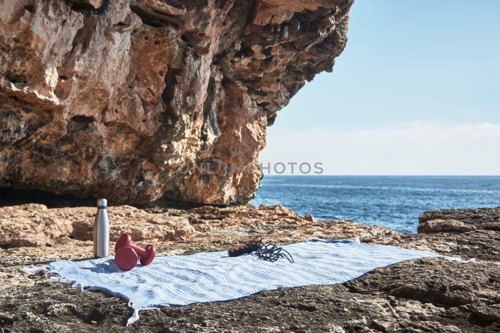 Fitness and sports concept background. Getting ready. Towel, jump rope, dumbbell and bottle of water, by the sea on a sunny winter day, with beautiful blue sky