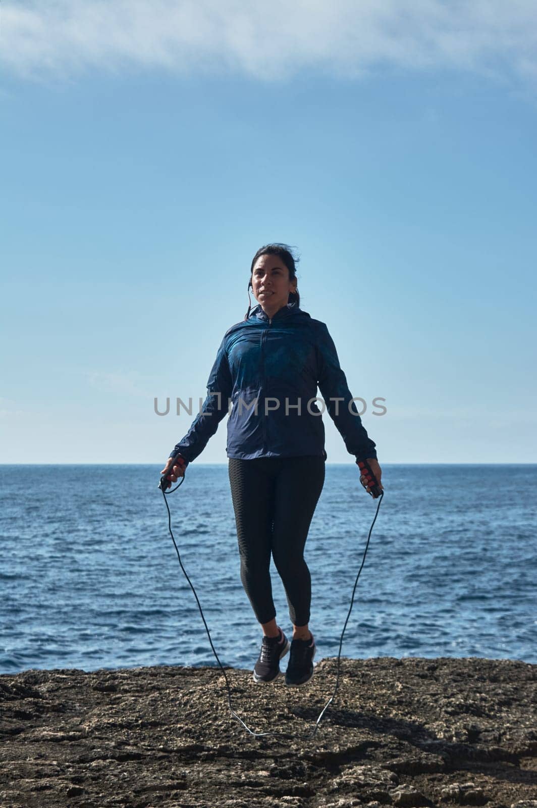 Latin woman, middle-aged, wearing sportswear, training, doing physical exercises, plank, sit-ups, climber's step, burning calories, keeping fit, outdoors by the sea, wearing headphones, smart watch