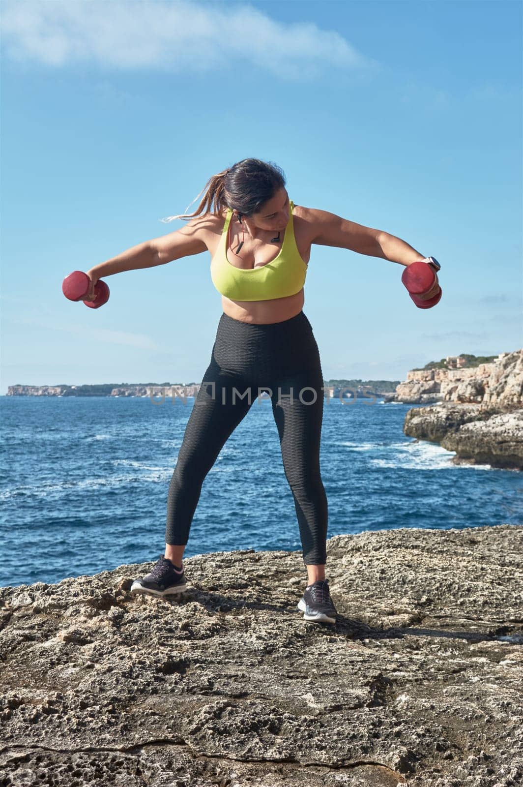 Latin woman, middle-aged, wearing sportswear, training, doing physical exercises, plank, sit-ups, climber's step, burning calories, keeping fit, outdoors by the sea, wearing headphones, smart watch