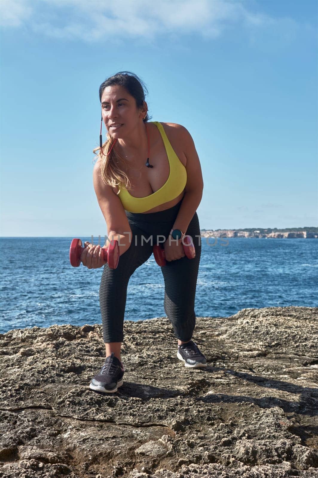 Latin woman, middle-aged, wearing sportswear, training, doing physical exercises, plank, sit-ups, climber's step, burning calories, keeping fit, outdoors by the sea, wearing headphones, smart watch
