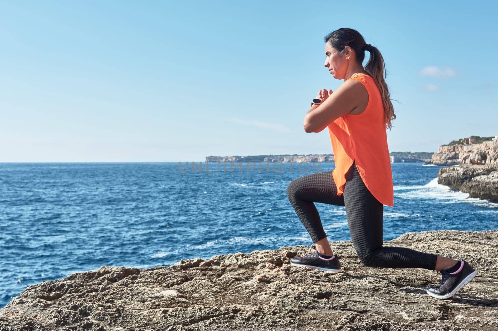 Latin woman, middle-aged, wearing sportswear, training, doing physical exercises, plank, sit-ups, climber's step, burning calories, keeping fit, outdoors by the sea, wearing headphones, smart watch