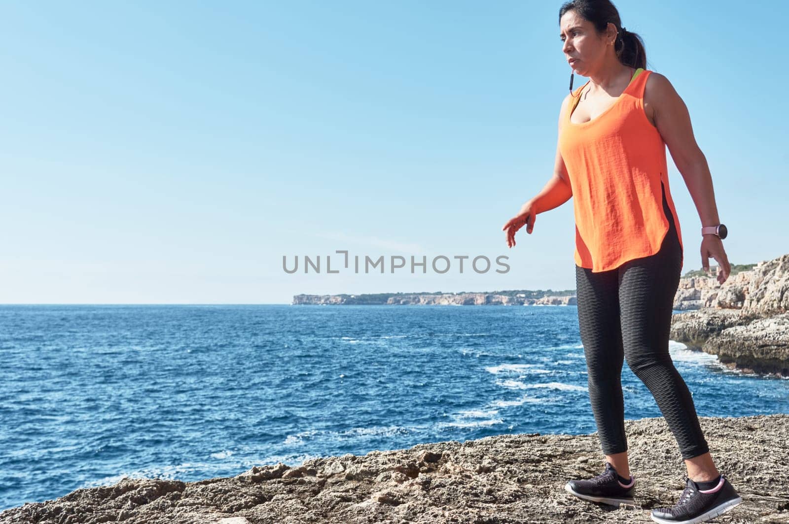 Latin woman, middle-aged, wearing sportswear, training, doing physical exercises, plank, sit-ups, climber's step, burning calories, keeping fit, outdoors by the sea, wearing headphones, smart watch