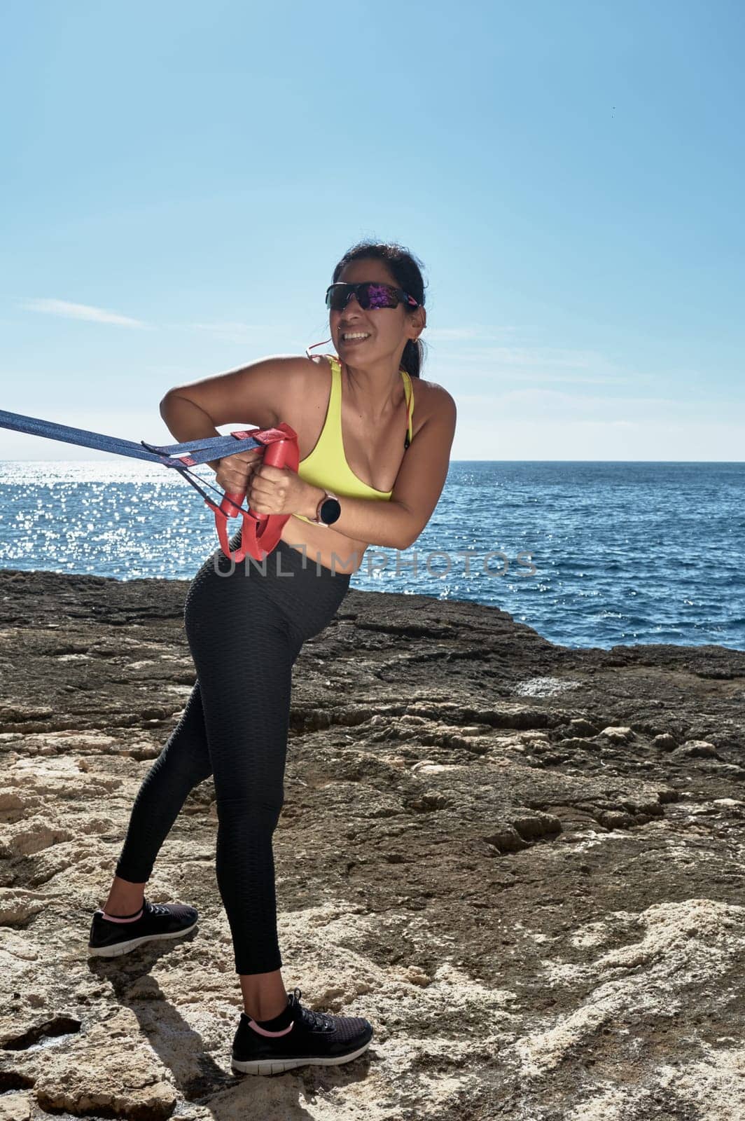 Latin woman, middle-aged, wearing sportswear, training, doing physical exercises, plank, sit-ups, climber's step, burning calories, keeping fit, outdoors by the sea, wearing headphones, smart watch