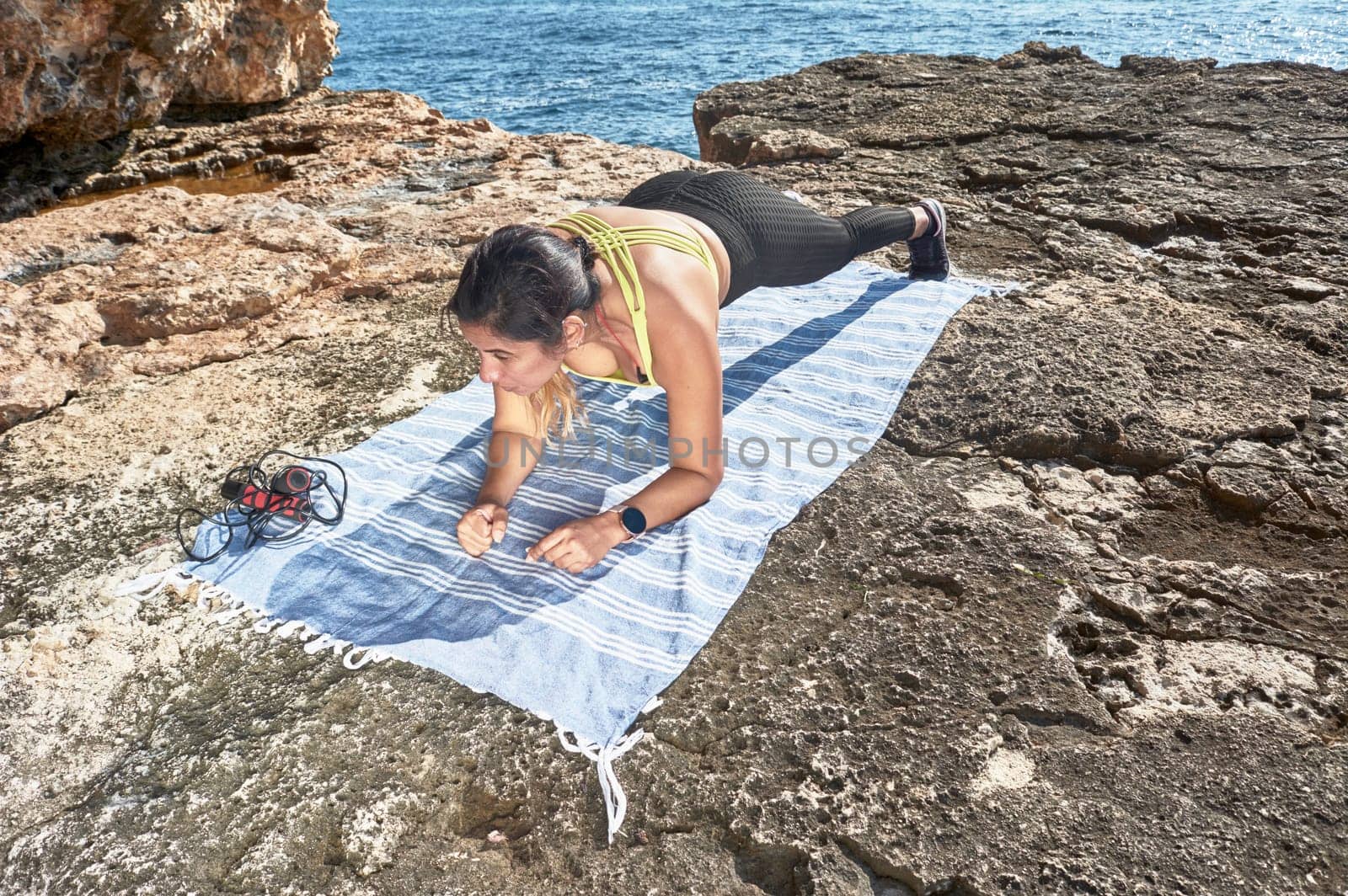FITNESS WOMAN IN SPORTS SET TRAINING WITH ELASTIC BAND, WEIGHTS, GYM EXERCISES, IN FRONT OF THE WATER.