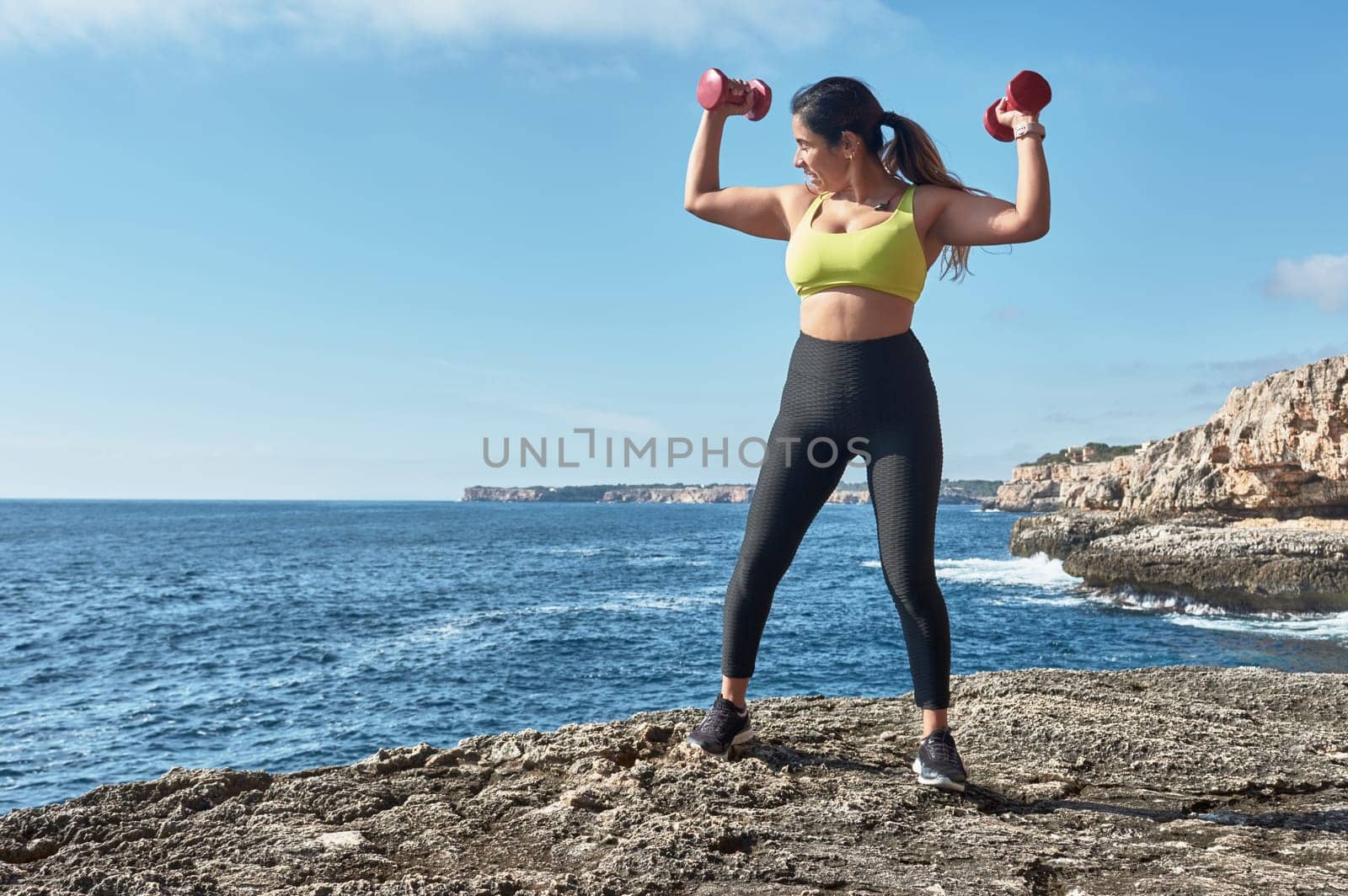 Latin woman, middle-aged, wearing sportswear, training, doing physical exercises, plank, sit-ups, climber's step, burning calories, keeping fit, outdoors by the sea, wearing headphones, smart watch