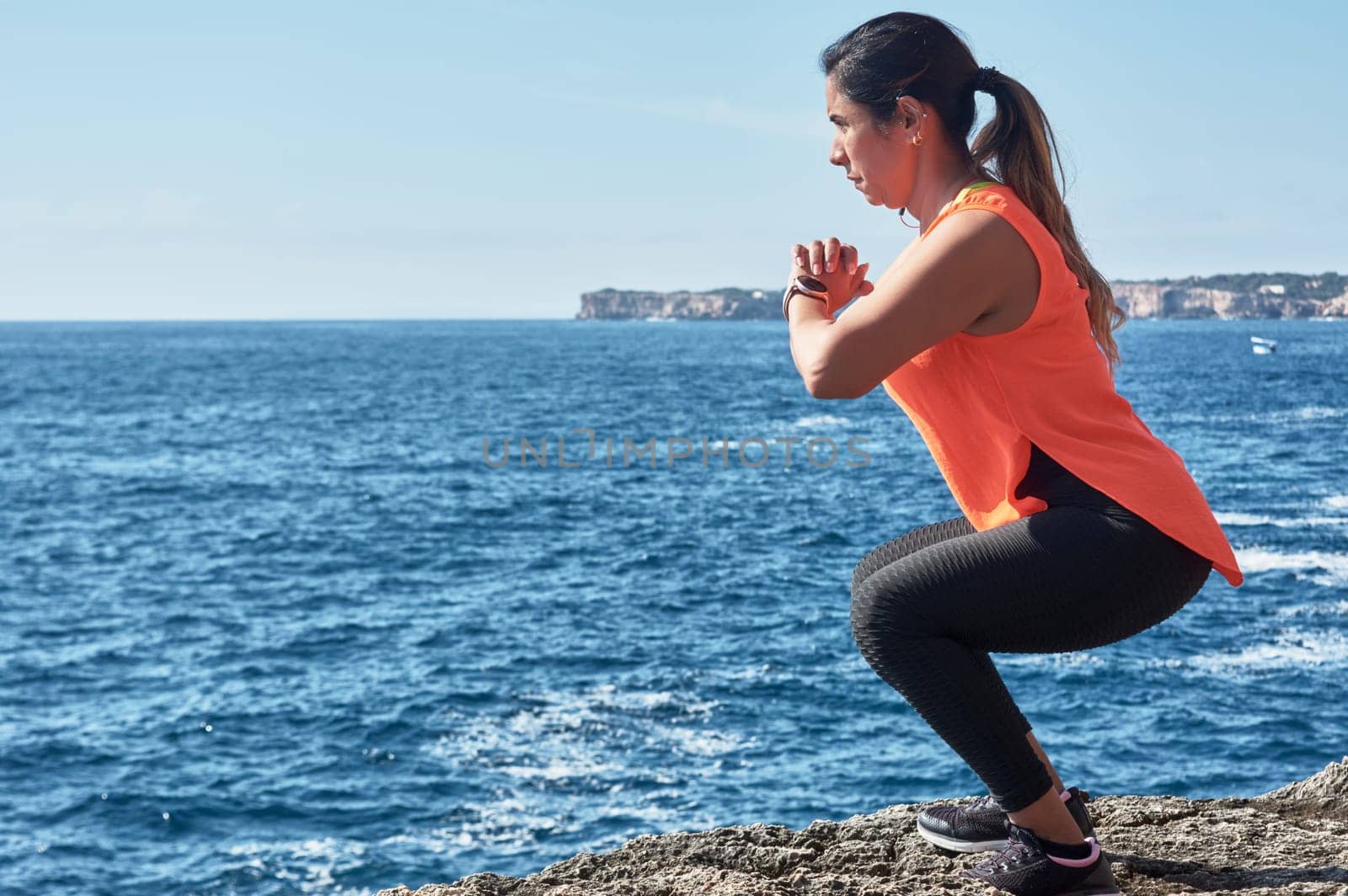 Latin woman, middle-aged, wearing sportswear, training, doing physical exercises, plank, sit-ups, climber's step, burning calories, keeping fit, outdoors by the sea, wearing headphones, smart watch