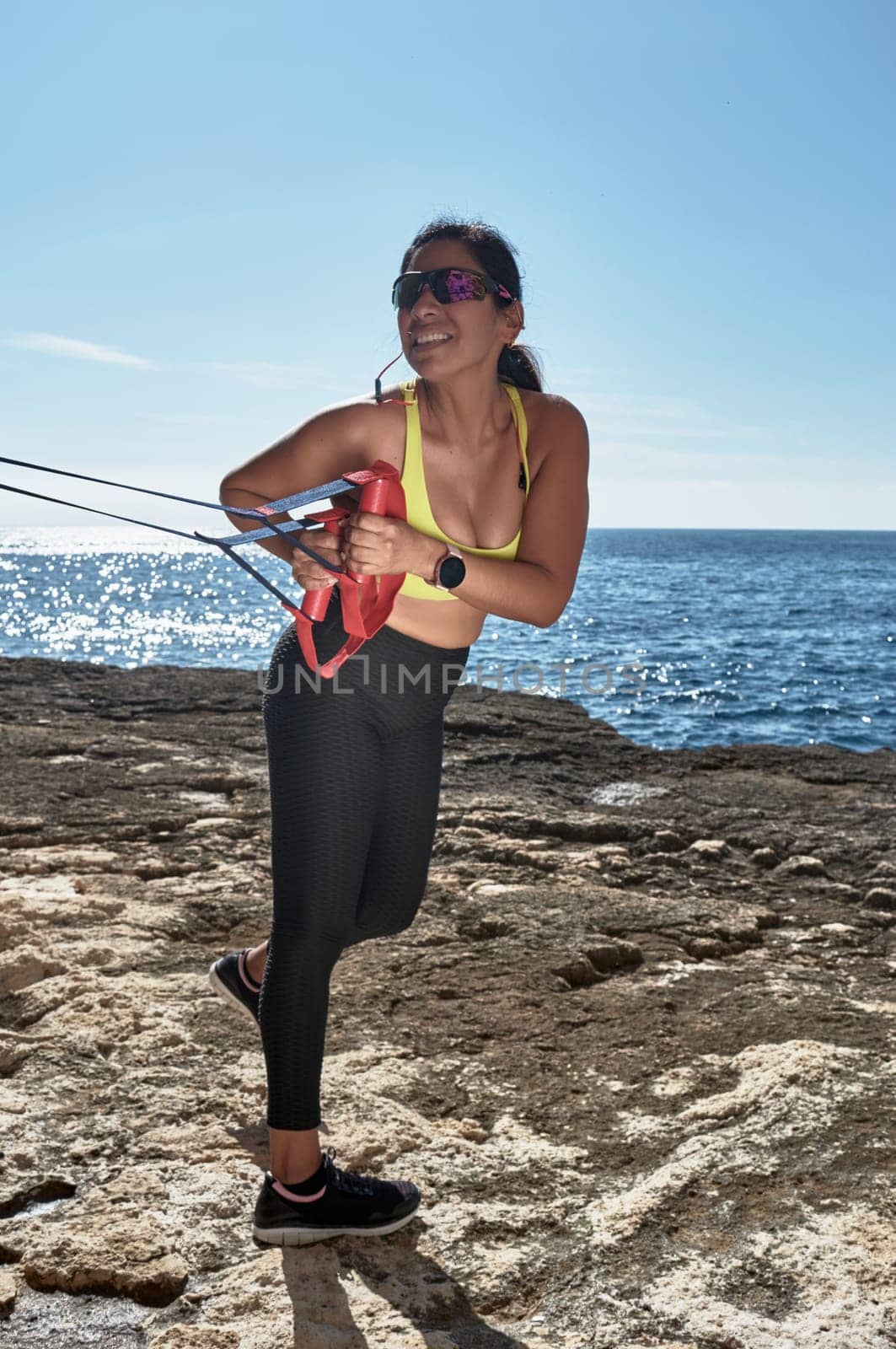 Latin woman, middle-aged, wearing sportswear, training, doing physical exercises, plank, sit-ups, climber's step, burning calories, keeping fit, outdoors by the sea, wearing headphones, smart watch
