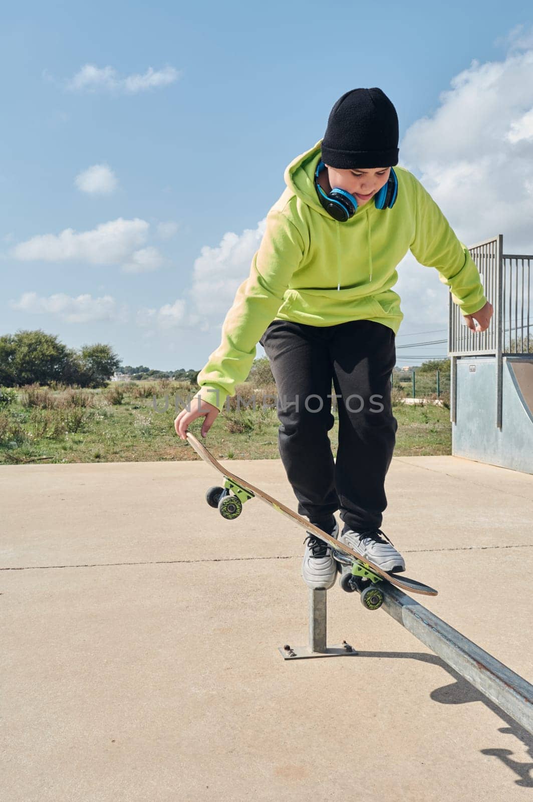 young, teenager, with a skateboard, holding the board with the hand, to jump, on a track, skateboarding, wearing headphones, green sweatshirt, black hat, swinging