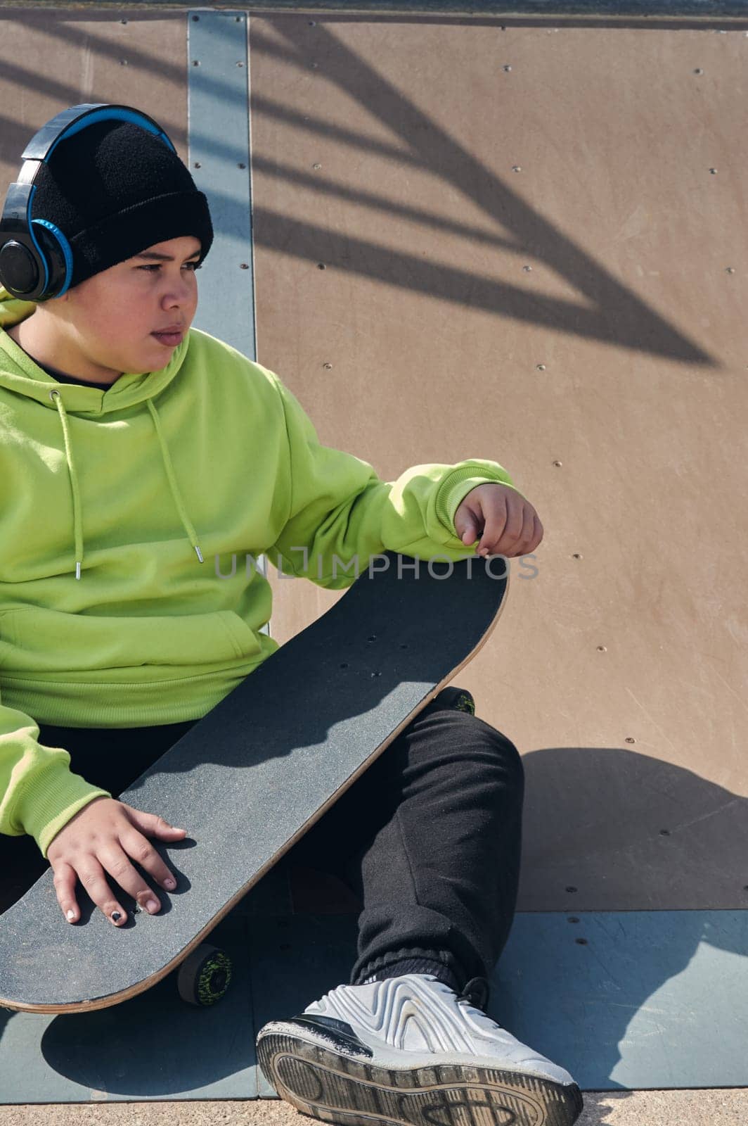 young man, teenager, skateboarding, sitting on the track, wearing headphones, green sweatshirt, black hat, thinking,