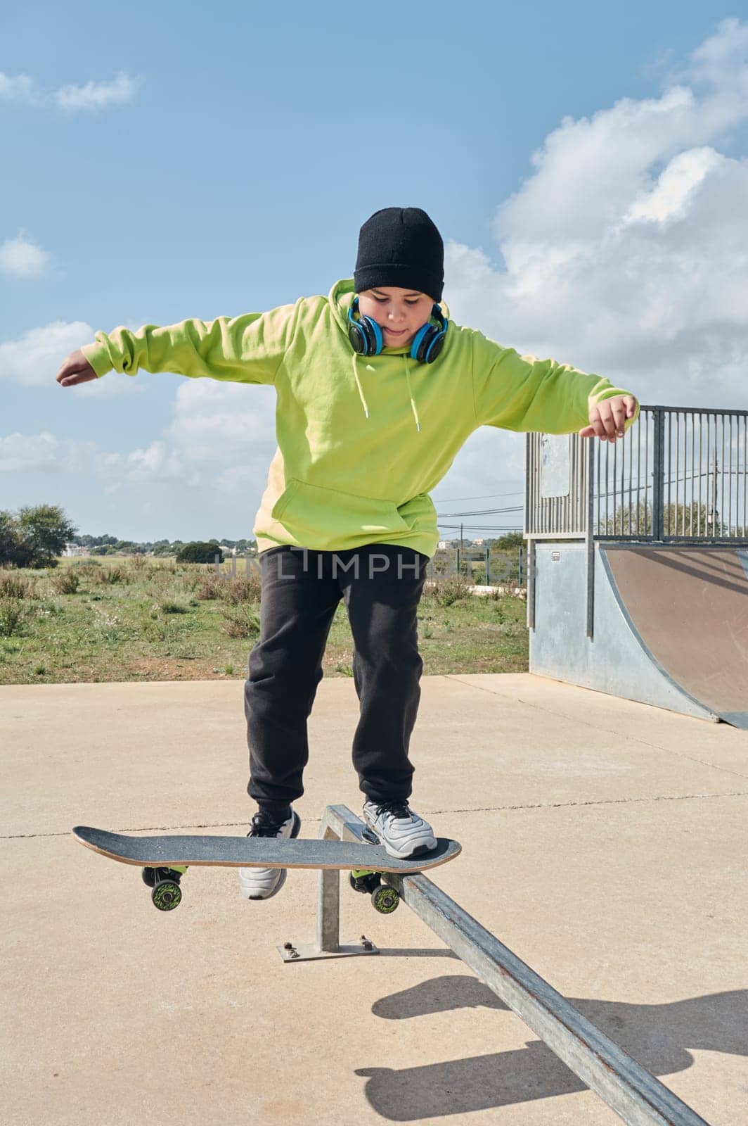 young, teenager, skateboarding, jumping, on the rink, wearing headphones, green sweatshirt, black hat, swinging