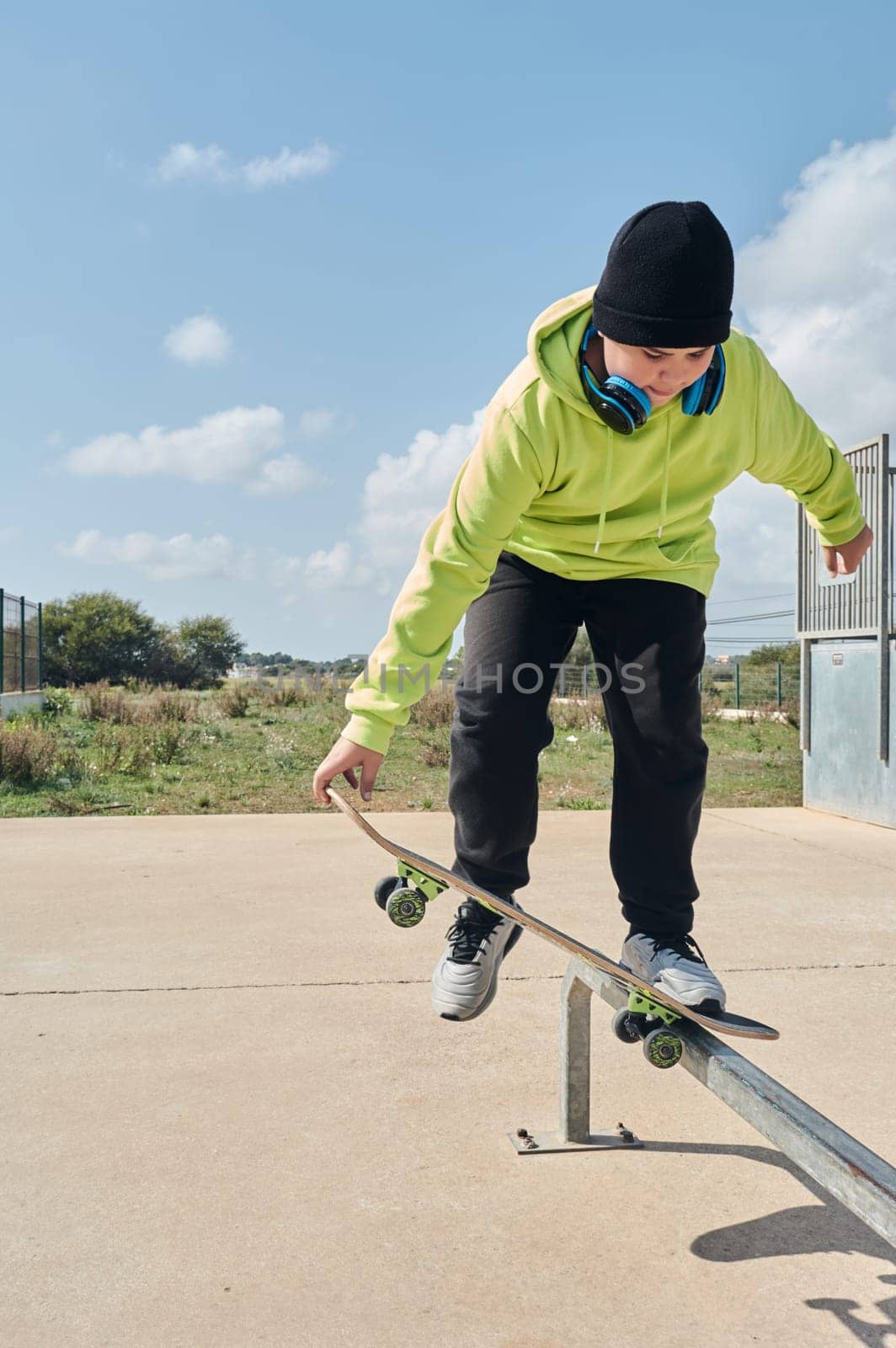 young, teenager, with a skateboard, holding the board with the hand, to jump, on a track, skateboarding, wearing headphones, green sweatshirt, black hat, swinging