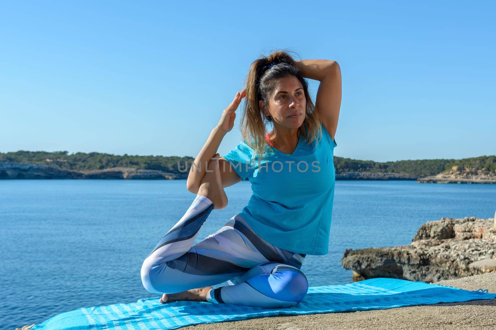 middle-aged fitness woman outdoors in front of the sea does yoga stretching exercises.