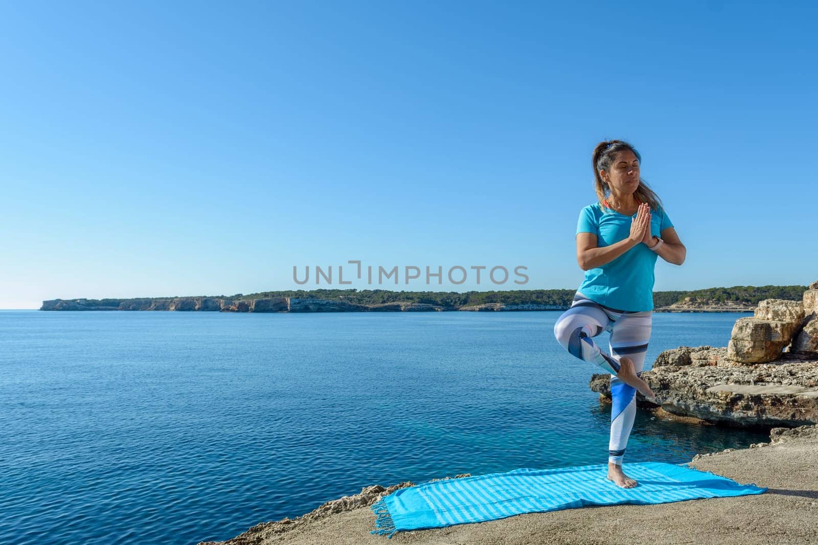 middle-aged fitness woman outdoors in front of the sea does yoga stretching exercises.