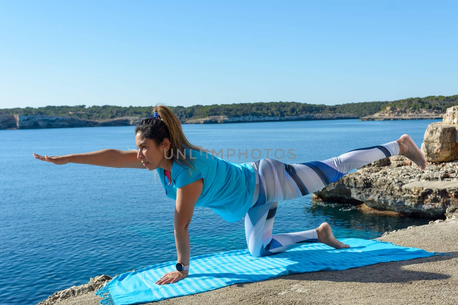 middle-aged fitness woman outdoors in front of the sea does yoga stretching exercises.