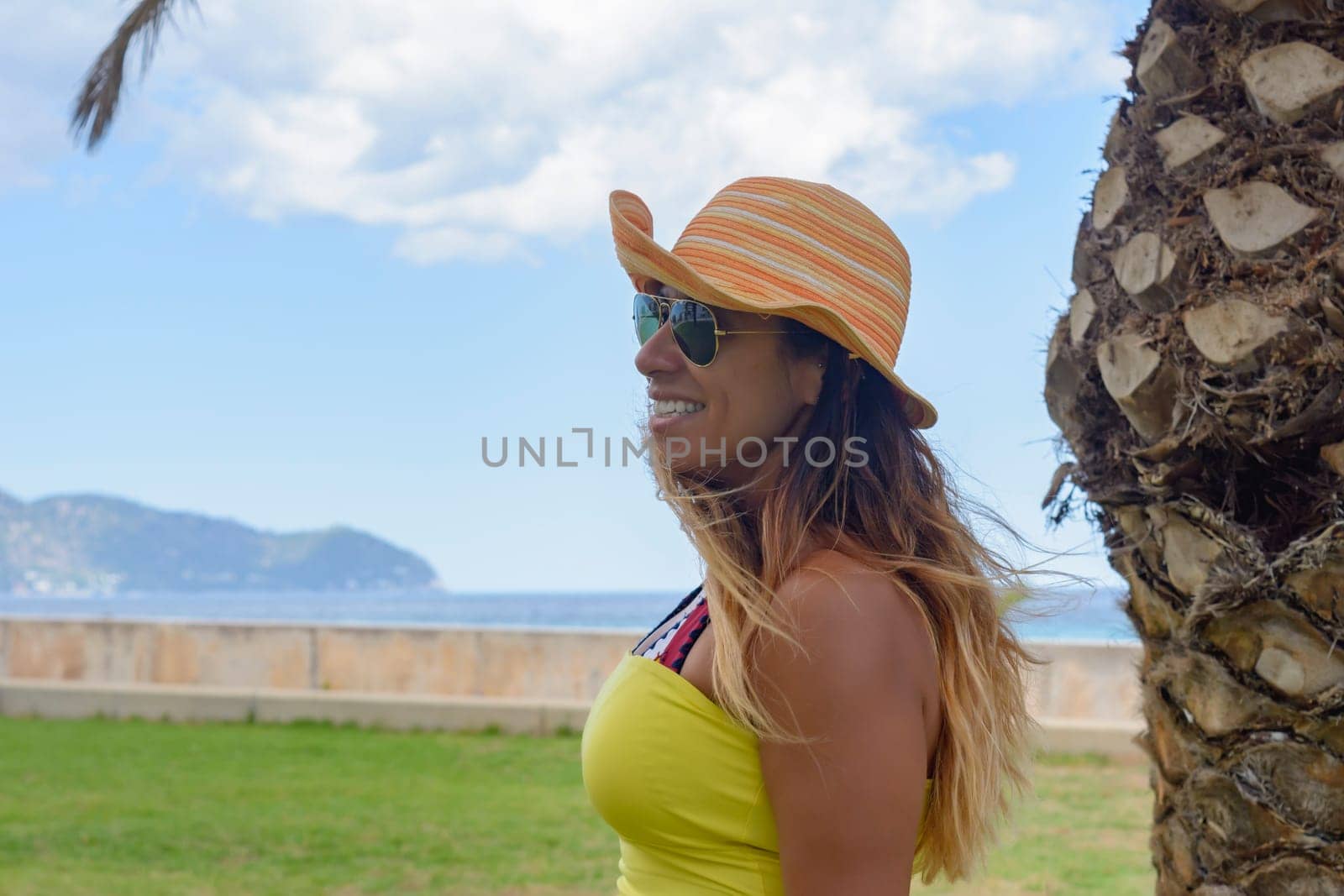 portrait of a latin woman smiling, having fun, on vacation in mallorca posing on a warm spring summer day, under a palm tree, hollidays concept,