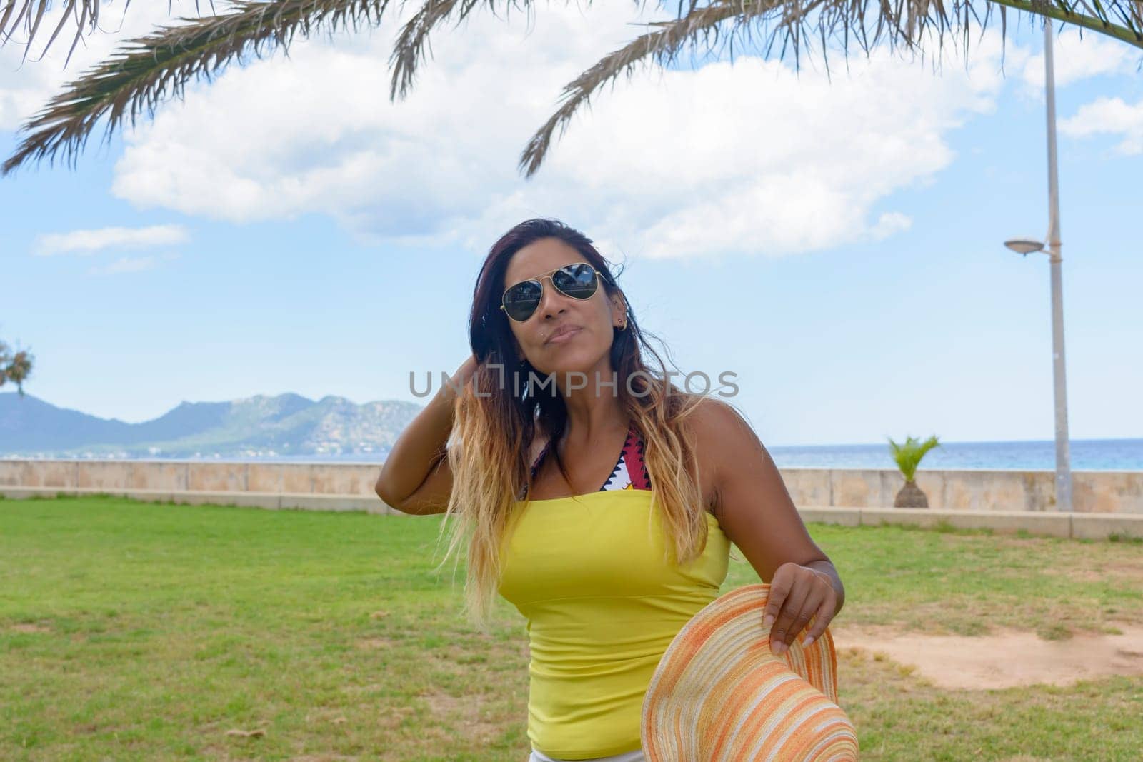 portrait of a latin woman smiling, having fun, on vacation in mallorca posing on a warm spring summer day, under a palm tree, hollidays concept,