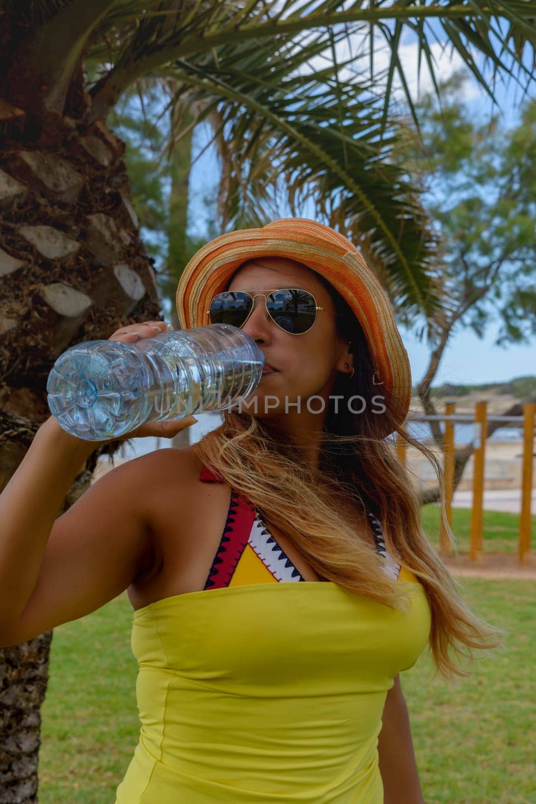 Happy woman drinking mineral water next to a palm tree enjoying the summer. Copyspace.