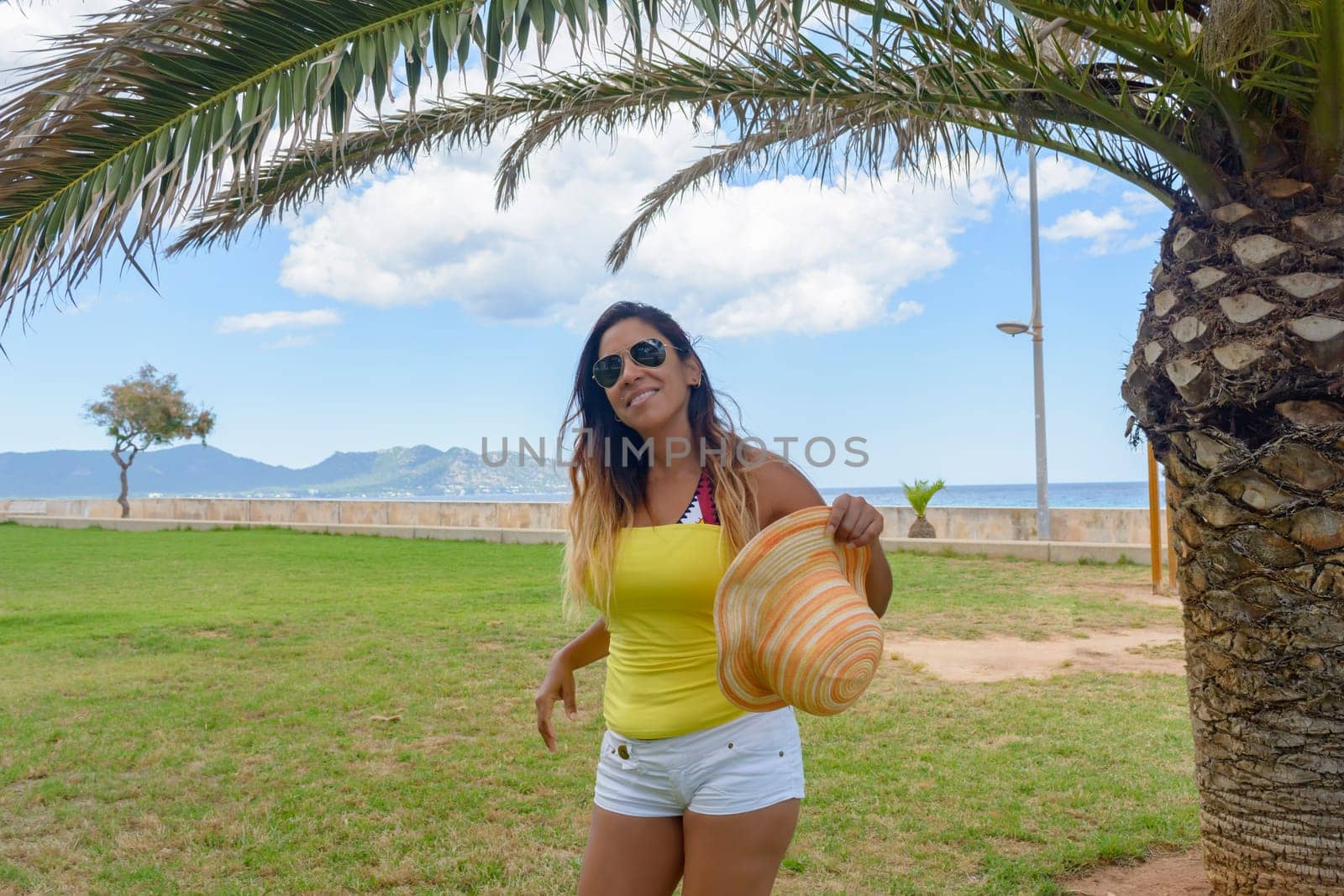 portrait of a latin woman smiling, having fun, on vacation in mallorca posing on a warm spring summer day, under a palm tree, hollidays concept,