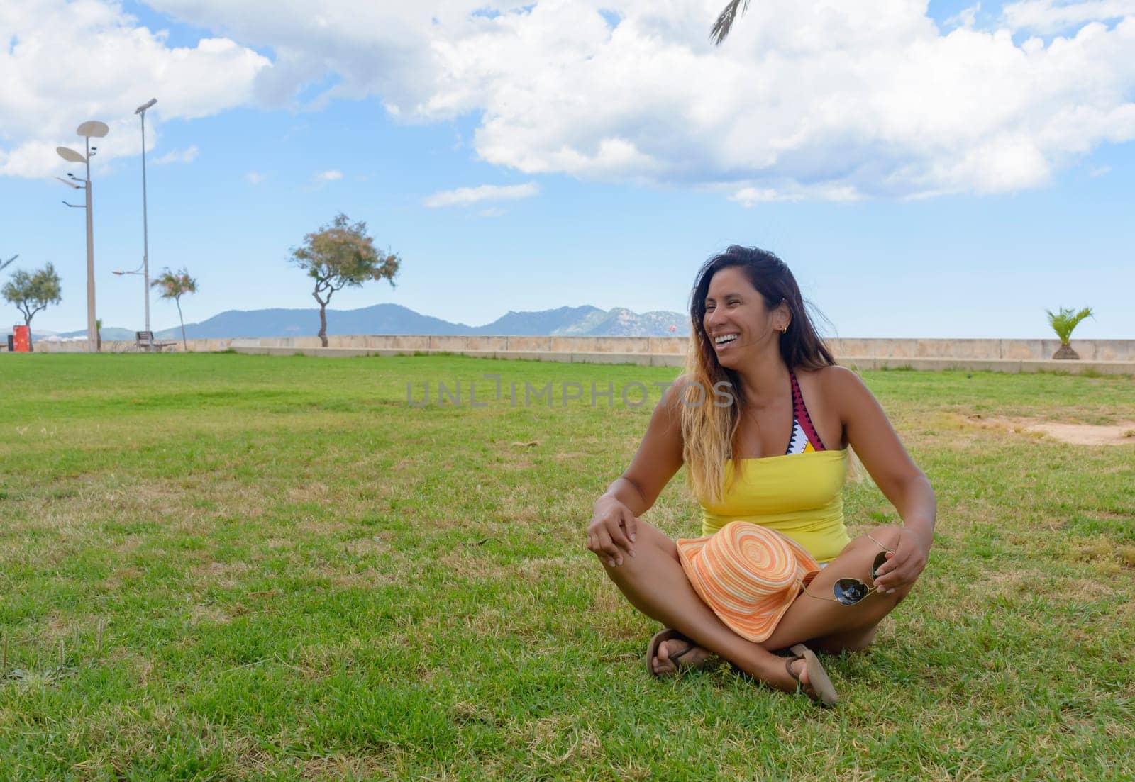 beautiful latin woman 40 years old, smiling sitting on the grass of a park in Mallorca, balearic islands, hollidays concept,