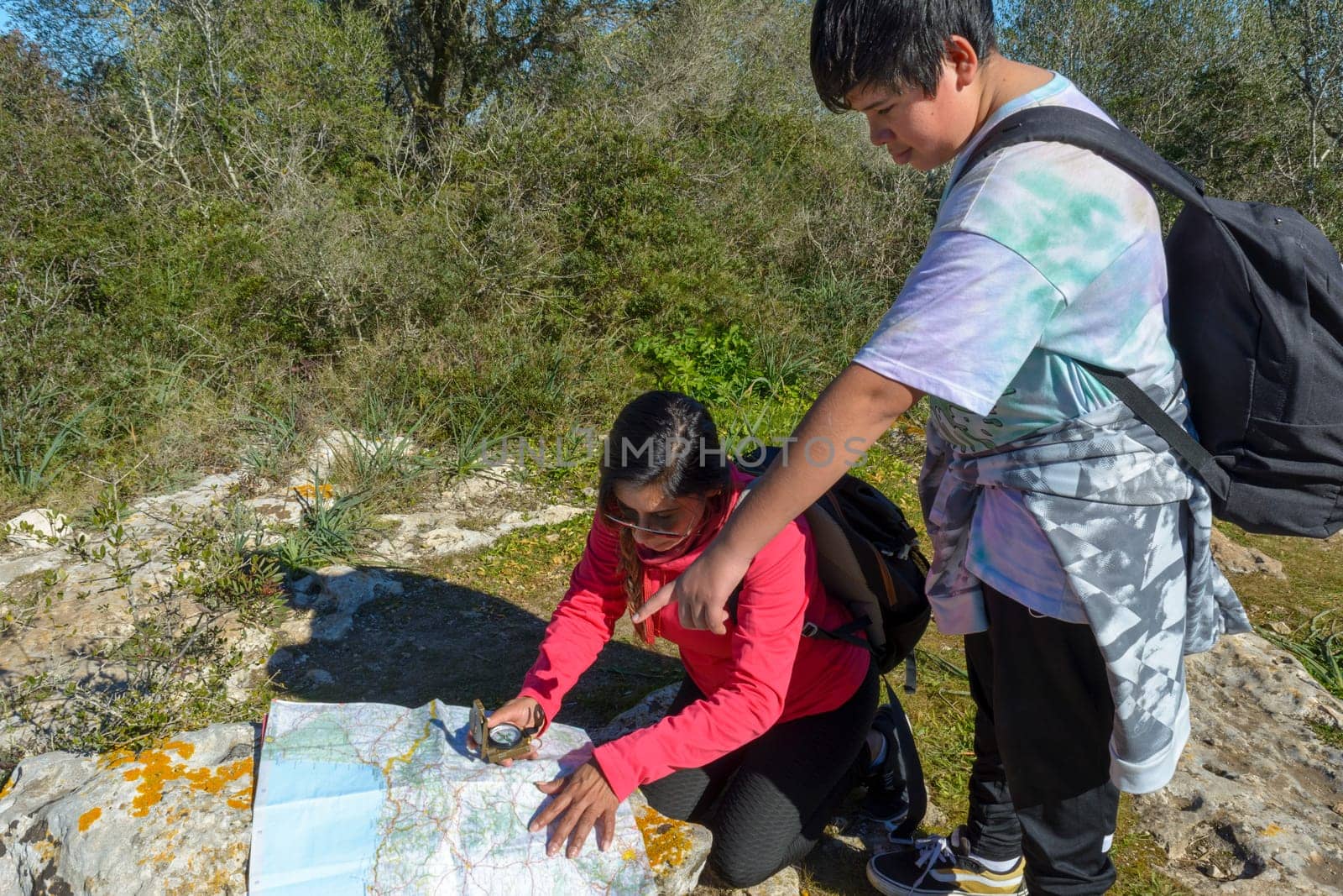 The boy and his mother are standing on top of the mountain. A woman travels with a child. Boy with his mother looking at a map. Travel with backpacks. Walk and climb with children.