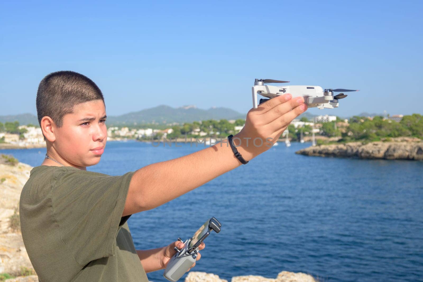 portrait happy teenage boy, preparing and finalizing flight details for drone flight, Mediterranean sea background on a sunny day, technology concept Spain, Balearic Islands