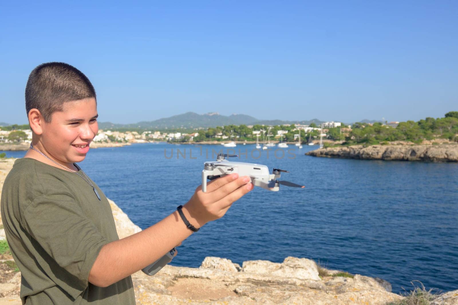 closeup, happy teenage boy, preparing for drone flight during sunny day with the sea in the background Spain, Balearic Islands