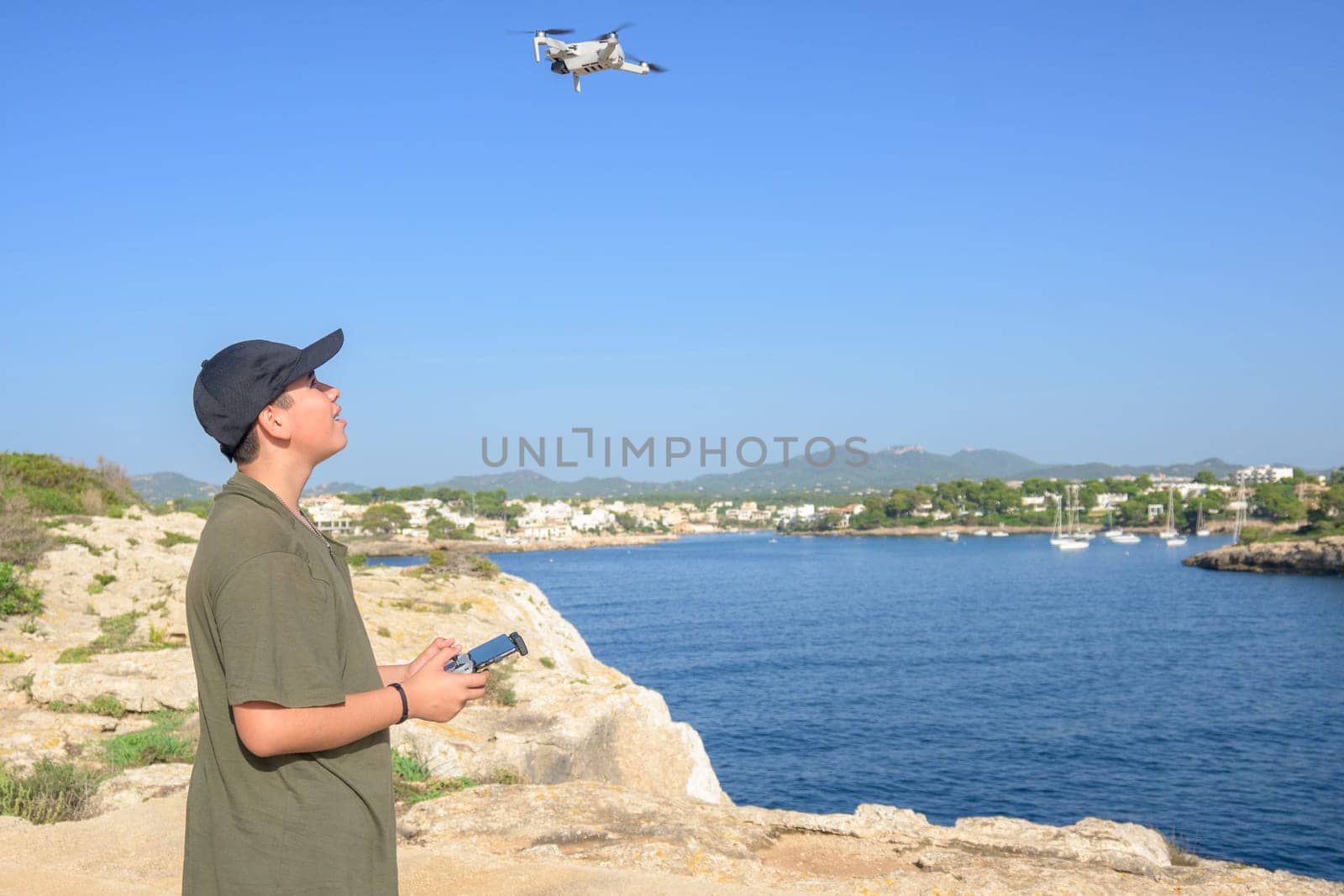 happy teen boy, flying drone on mediterranean coast, against blue sky during sunny day Spain, Balearic Islands