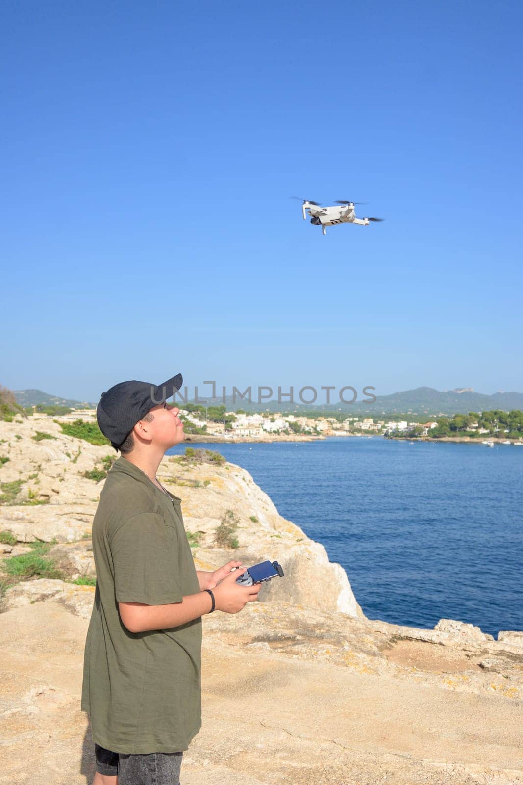 happy teen boy, flying drone on mediterranean coast, against blue sky during sunny day Spain, Balearic Islands