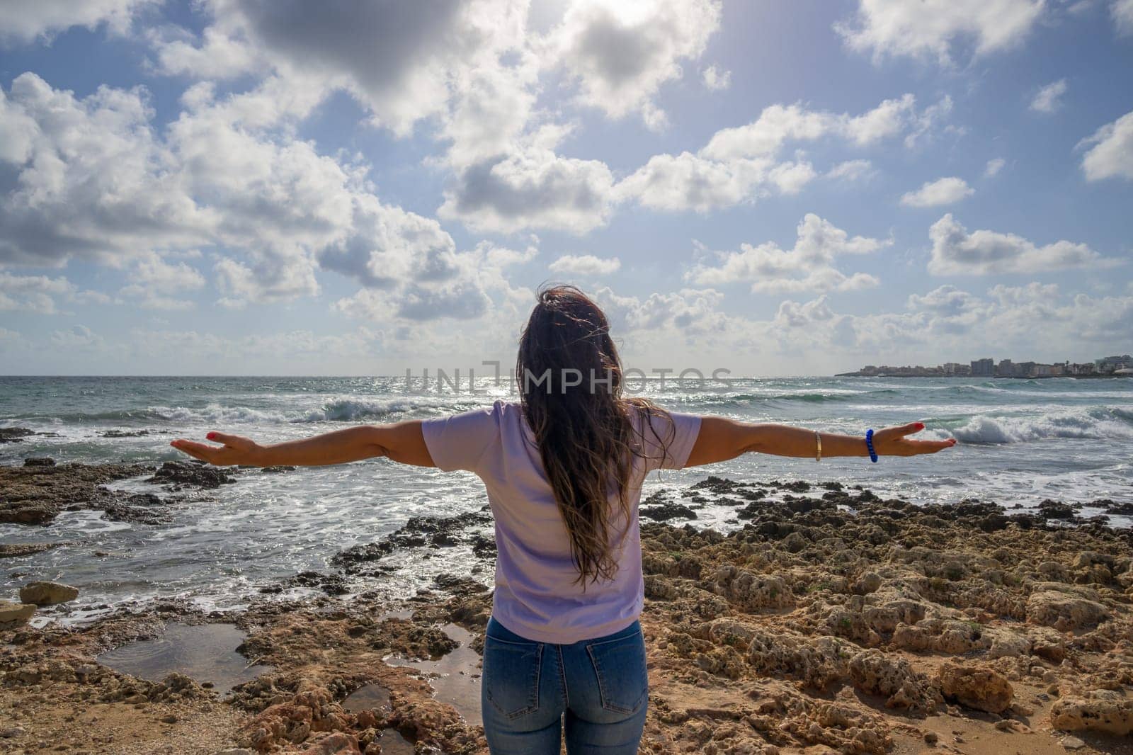 Happy woman celebrating her holiday in front of the Mediterranean Sea in a coastal landscape.