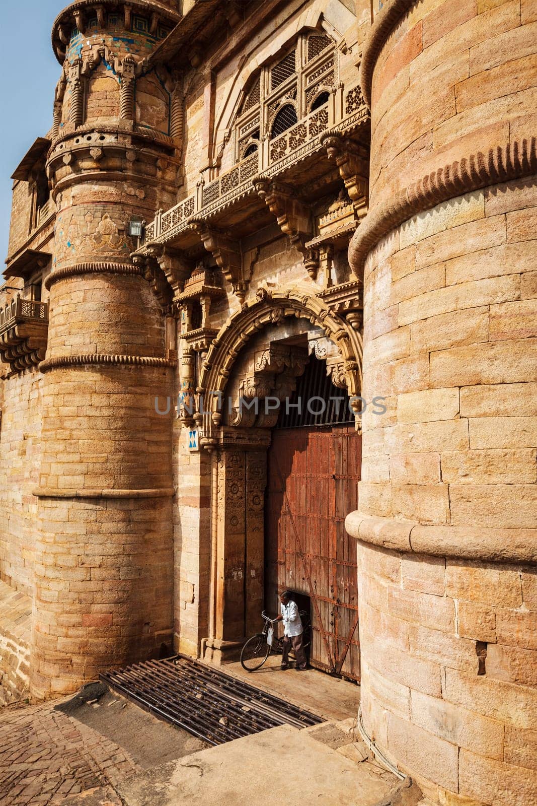 GWALIOR, INDIA - APRIL 11, 2011: Man with bicycle coming through door in huge gates of Gwalior Fort - 8th-century hill fort that houses many historic monuments including palaces, temples and water tanks