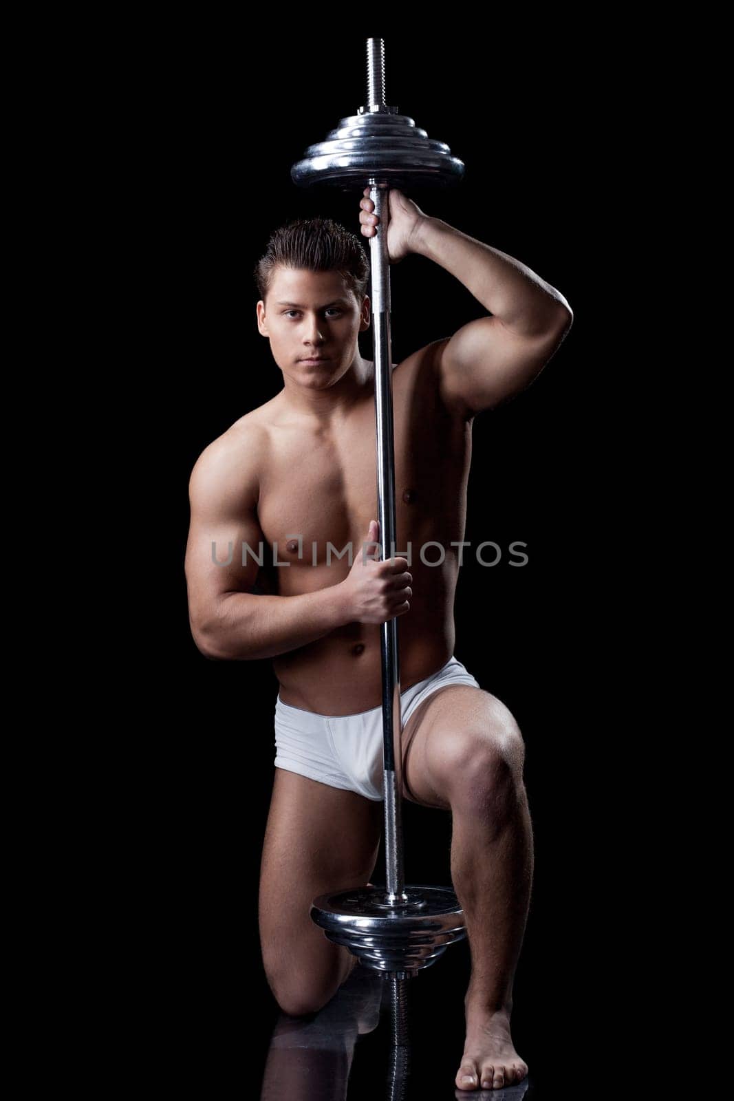 Attractive muscular man posing with barbell, isolated on black